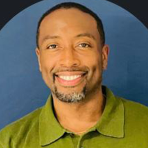 A man smiling, wearing a green collared shirt, posing against a blue background.